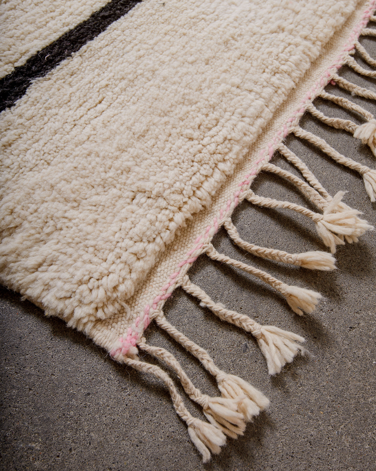 Corner of rug made of thick cream wool and natural wool tassels.
